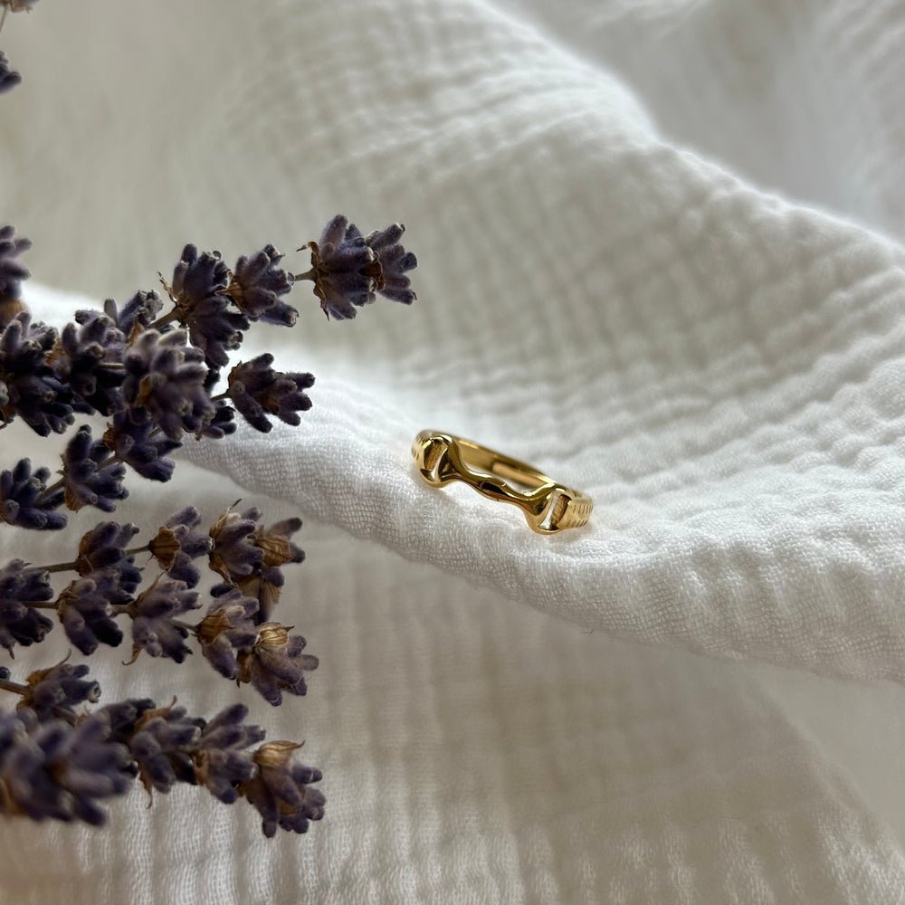 The Ana Ring, featuring a unique design, rests on textured white fabric with a sprig of dried lavender placed to its left.