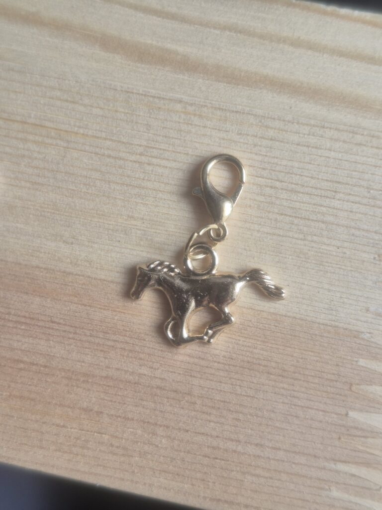The Lucky Charm Keyring features a small gold galloping horse with a lobster clasp, perfect for attaching to your favourite keyring and shown resting on a light wooden surface.