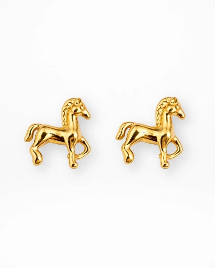 A pair of Tiny Horse Earrings in a small, gold-tone design showcased on a white background. Each earring depicts a horse with one front leg lifted and is accented with a flowing mane.