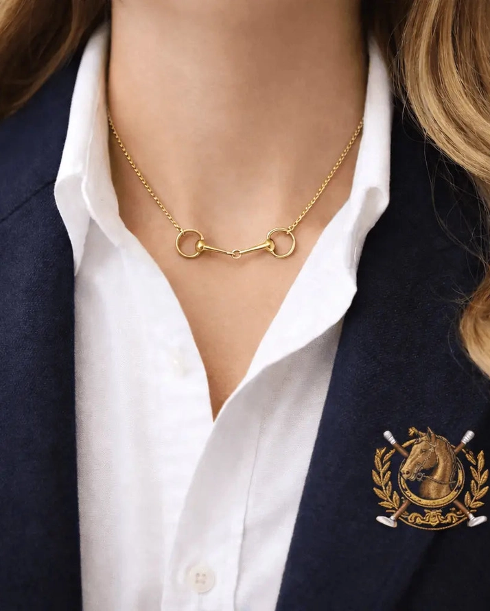 Wearing a stylish Snaffle Bit Necklace—a perfect piece of equestrian jewellery—paired with a crisp white collared shirt and a navy blazer featuring an embroidered gold horse crest creates an elegant and sophisticated look, making it an ideal gift for any horse lover.