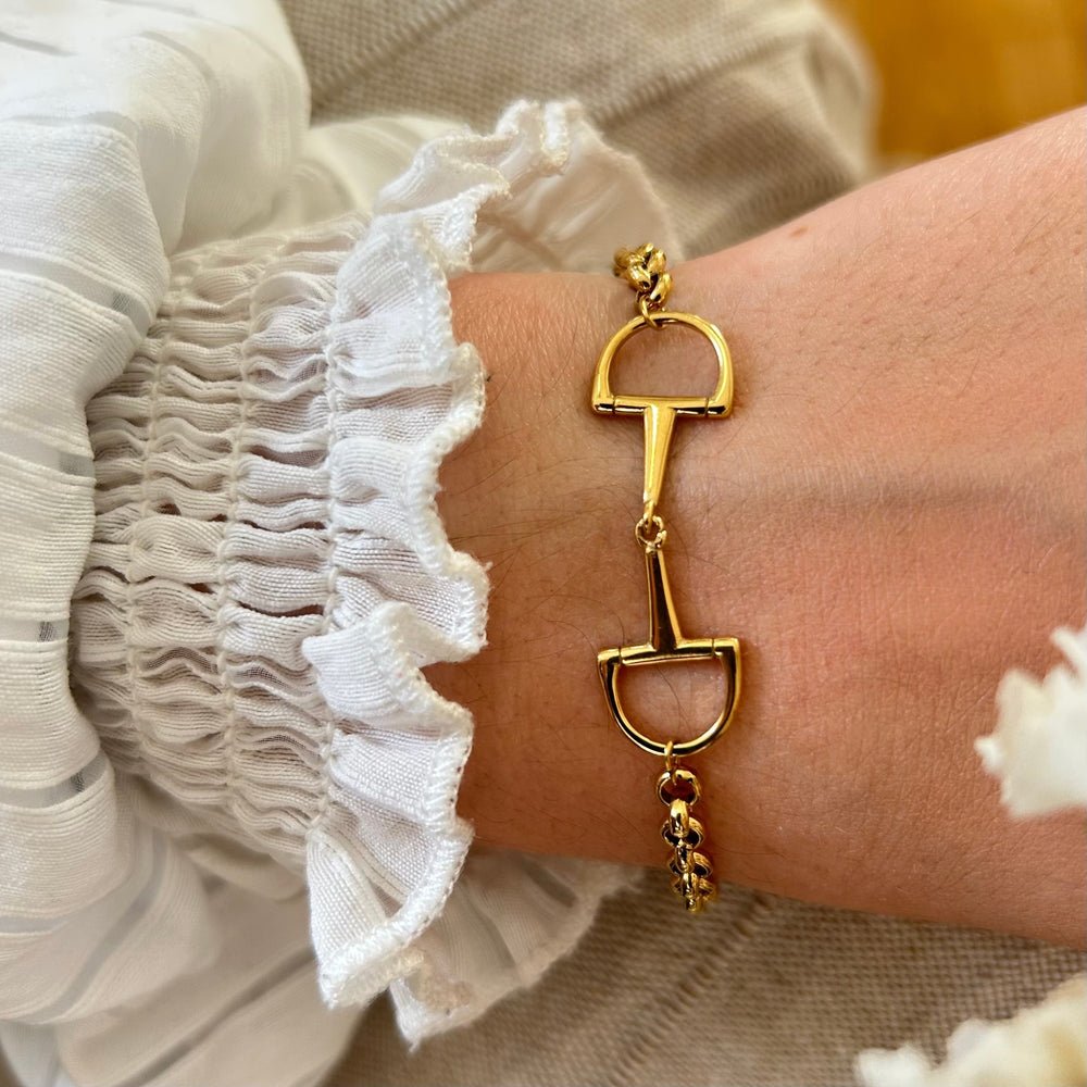 A gold bracelet with a horse bit centrepiece worn on a wrist.