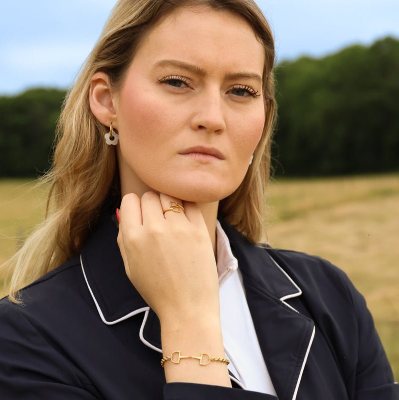 A woman wearing a gold ring and a gold snaffle-bit bracelet.