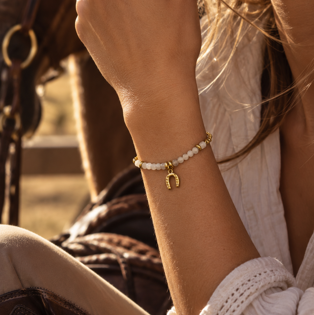 A beaded bracelet with a gold horseshoe charm on a person's wrist.